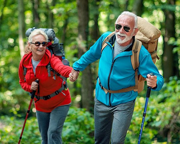 Ein glückliches Seniorenpaar in Sportkleidung wandert durch den Wald.