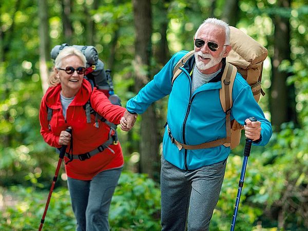 Ein glückliches Seniorenpaar in Sportkleidung wandert durch den Wald.