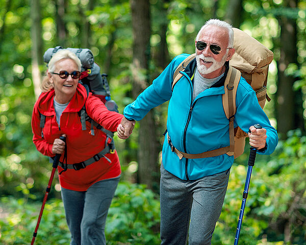 Ein glückliches Seniorenpaar in Sportkleidung wandert durch den Wald.