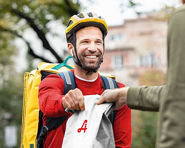 Fahrradbote überreicht Tüte mit Bestellung an Kunden.