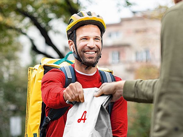 Fahrradbote überreicht Tüte mit Bestellung an Kunden.