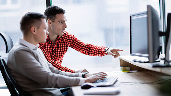 Zwei Geschäftsmänner sitzen in einem Büro und arbeiten gemeinsam fokussiert am Computer.
