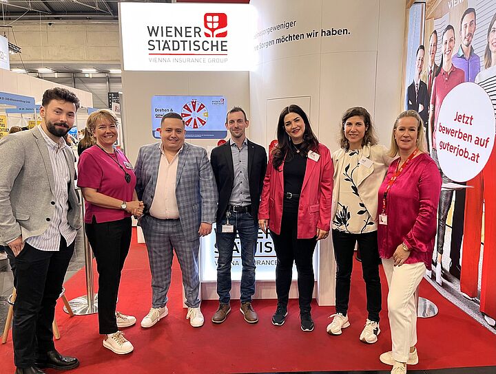 Gruppenfoto von sieben Personen auf einer Jobmesse vor einem Messestand mit digitalem Glücksrad.