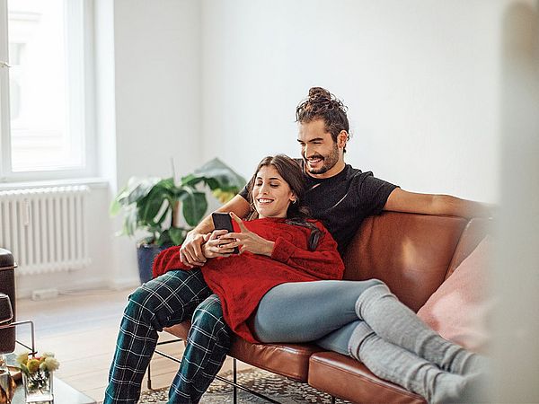 Eine junge Frau liegt auf dem Schoß ihres Partners und beide blicken auf ihr Smartphone.