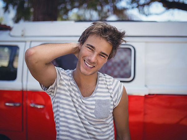 Ein junger Mann lächelt in die Kamera und steht dabei vor einem Kleinbus 