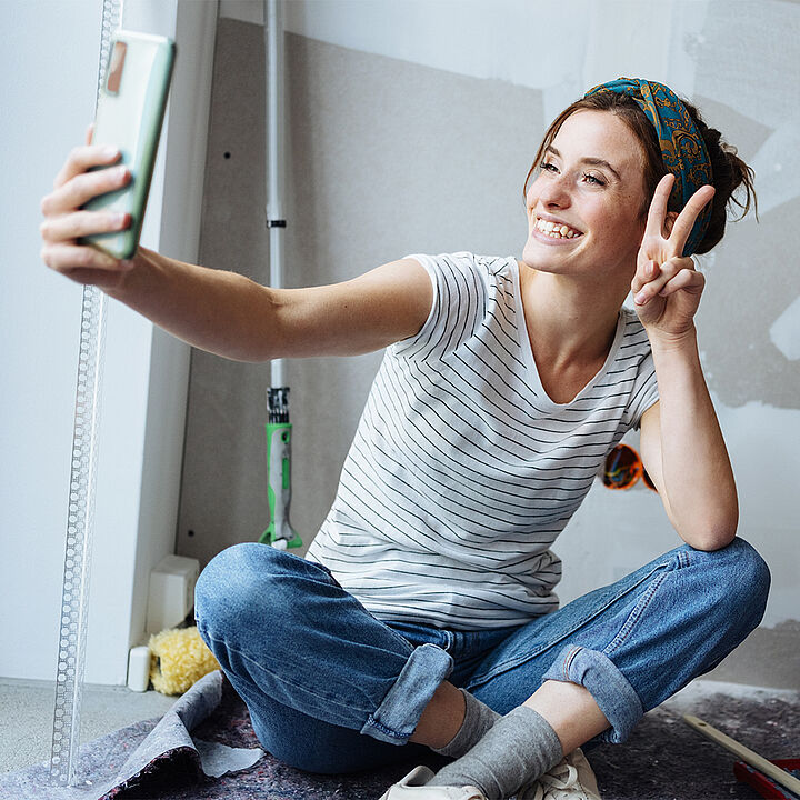 Junge Frau mit Haarband macht mit den Fingern das Victory Zeichen und macht ein Selfie von sich.