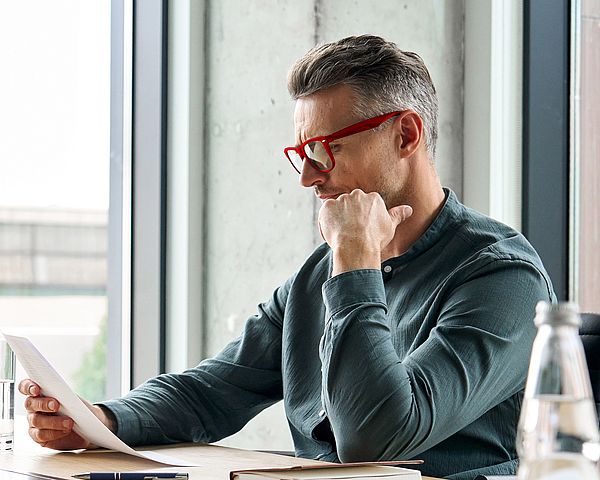 Ein Mann mit Brille liest konzentriert am Schreibtisch.