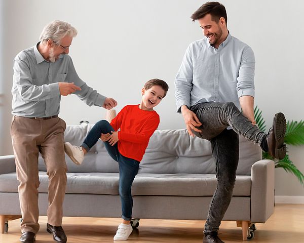 Drei glückliche Männer verschiedener Generationen tanzen im Wohnzimmer.