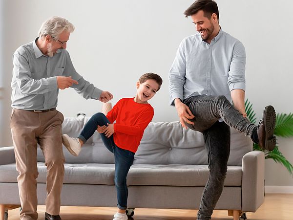 Drei glückliche Männer verschiedener Generationen tanzen im Wohnzimmer.