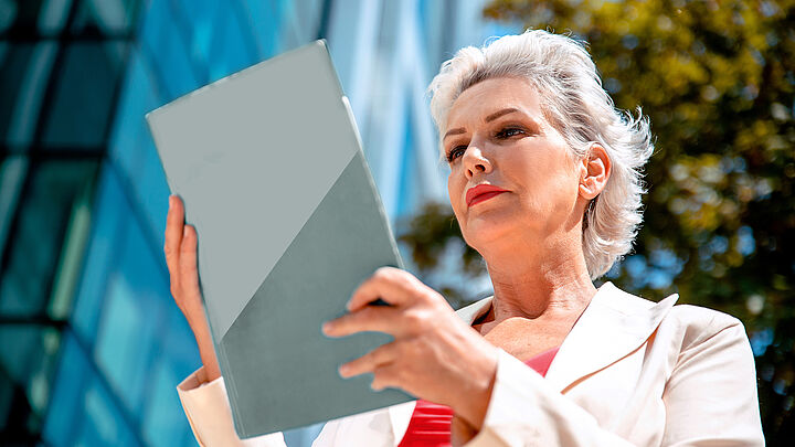 Eine Frau liest ein Aktendokument vor einem Gebäude.