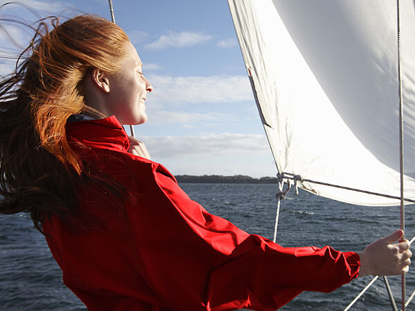 Eine junge Frau steht auf einem Segelschiff und genießt den Sonnenschein.
