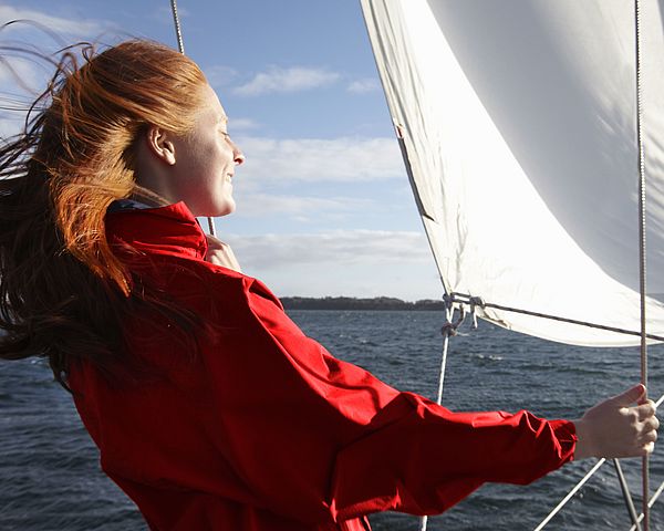 Eine junge Frau steht auf einem Segelschiff und genießt den Sonnenschein.
