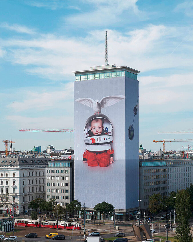 Foto vom Ringturm, wo die Fassade mit einer Abbildung eines Kindes mit Weltraumhelm und Taube tapeziert ist.  