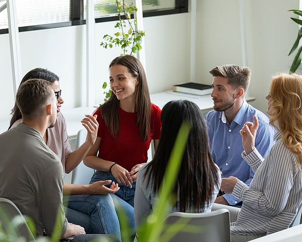 Eine Gruppe von jungen Leuten sitzt im Büro im Kreis und bespricht etwas.