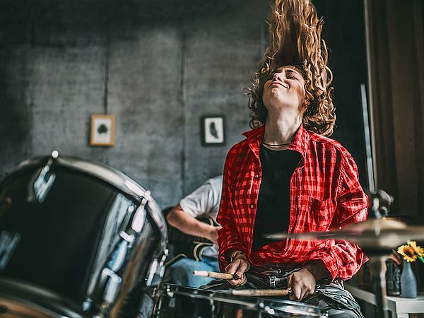 Eine junge Frau spielt am Schlagzeug und wirft dabei ihre Haare nach hinten.