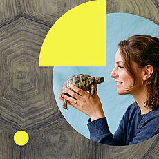 Junge Frau mit braunen, lockigen Haaren im Profil, die lächelnd eine kleine Landschildkröte in beiden Händen hält.