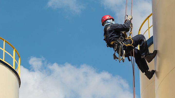 Ein Arbeiter klettert an einem Seil gesichert auf einem Speichertank.