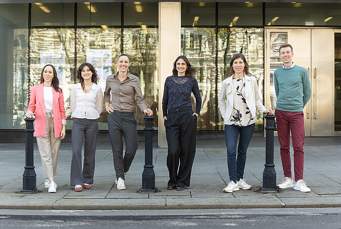 Fünf Frauen und ein Mann stehen lässig am Straßenrand und blicken alle lächelnd Richtung Kamera
