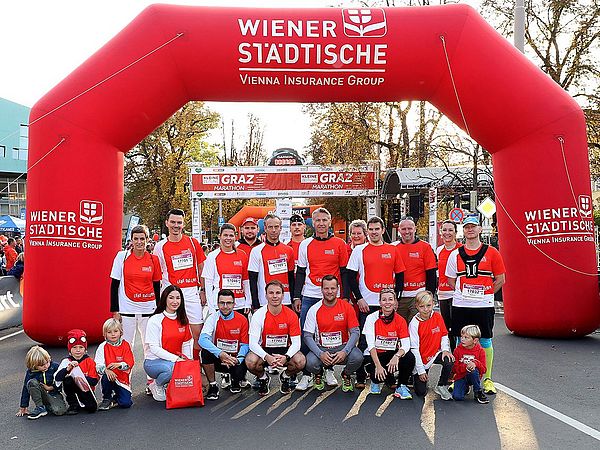 Eine Gruppe von Teilnehmerinnen und Teilnehmern steht nach absolvierten Graz Marathon im Ziel und jubelt voller Freude  