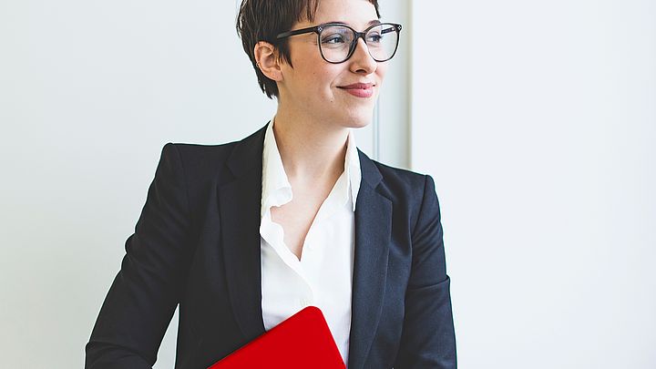 Eine Geschäftsfrau mit Brille hält ihren Laptop und lächelt dabei
