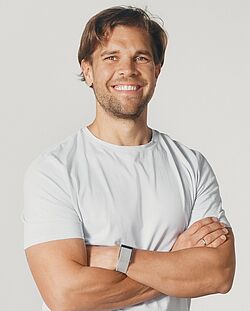 Porträtfoto eines Mannes mit verschränkten Armen und einem Lächeln, der ein weißes T-Shirt und eine Smartwatch trägt.