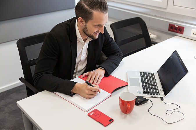 Mitarbeiter sitzt an Schreibischt und arbeitet am Laptop.