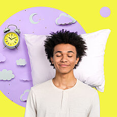 Ein strubbeliger junger Mann mit geschlossenen Augen steht lächelnd vor einem Kopfpolster und einem Wecker mit neongelbem Zifferblatt.