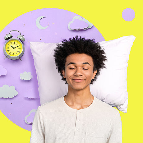 Ein strubbeliger junger Mann mit geschlossenen Augen steht lächelnd vor einem Kopfpolster und einem Wecker mit neongelbem Zifferblatt.