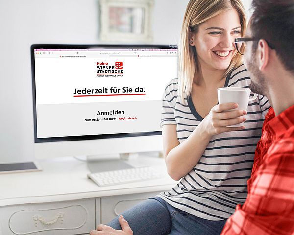 Ein junges Paar lächelt sich an, während im Hintergrund am PC das Kundenportal geöffnet ist.
