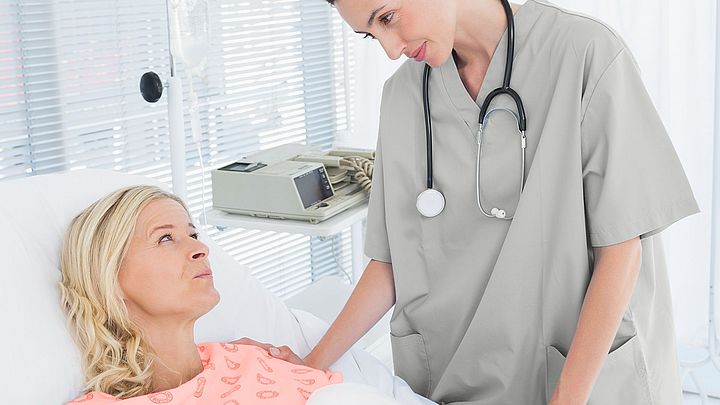 Eine Ärztin kümmert sich um eine Patientin im Krankenhaus, welche im Krankenbett liegt.