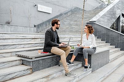 Ein Mann und eine Frau sitzen auf den Stiegen und unterhalten sich.