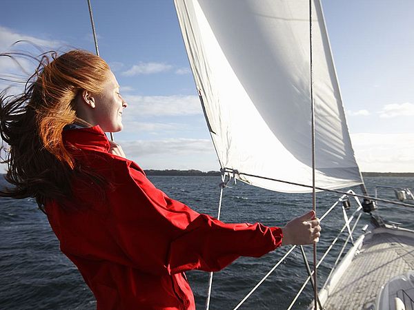 Eine junge Frau steht auf einem Segelschiff und genießt den Sonnenschein.