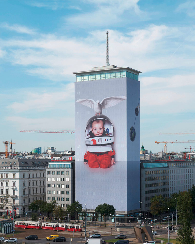 Foto vom Ringturm, wo die Fassade mit einer Abbildung eines Kindes mit Weltraumhelm und Taube tapeziert ist.  