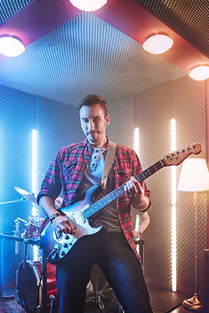 Ein Mann mit Gitarre steht auf der Bühne und lächelt zum Publikum. Im Hintergrund ist eine Band zusehen. 