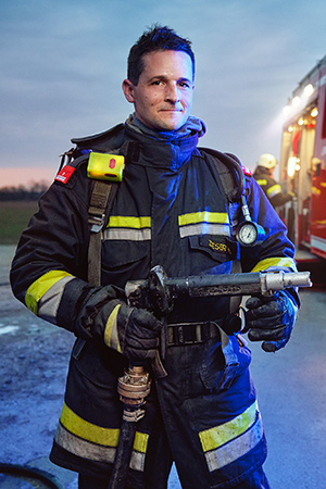 Ein Feuerwehrmann mit Wasserschlauch steht auf einem Feld neben einem Feuerwehrauto 