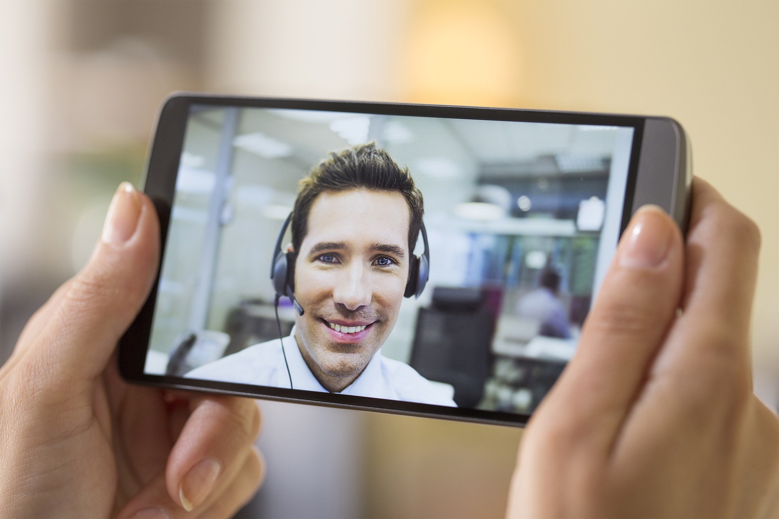 Eine Frau hält ein Smartphone in der Hand, worüber eine Videokonferenz mit einem Berater stattfindet  